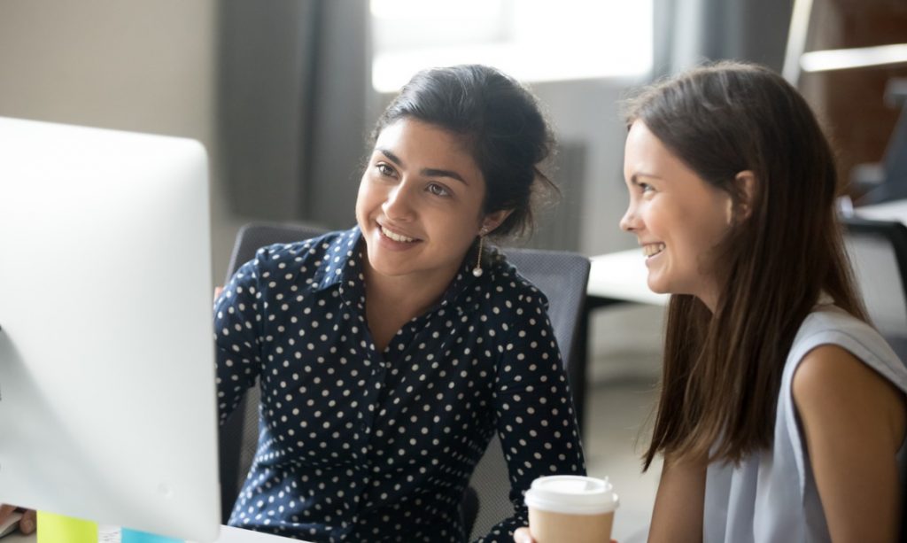 smiling-diverse-female-interns-talking-in-office-discussing-online-picture-id1070271482