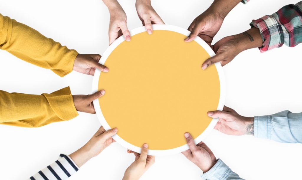 diverse-hands-supporting-a-blank-yellow-round-board-picture-id1125541252